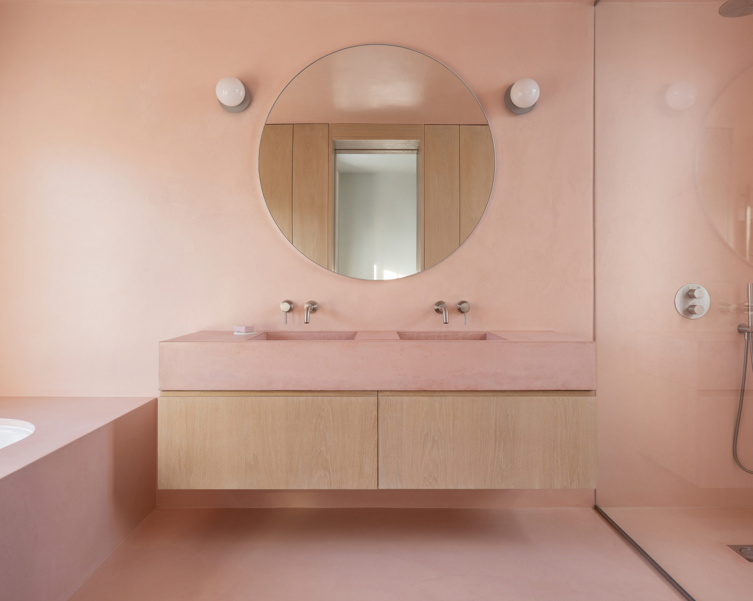 Double sink and mirror in bathroom with bespoke cabinet. Pink micro cement walls.