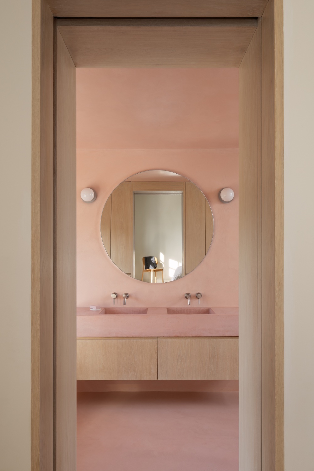 View into bathroom showing double sink round mirror 2 wall lights. Pink micro cement walls.